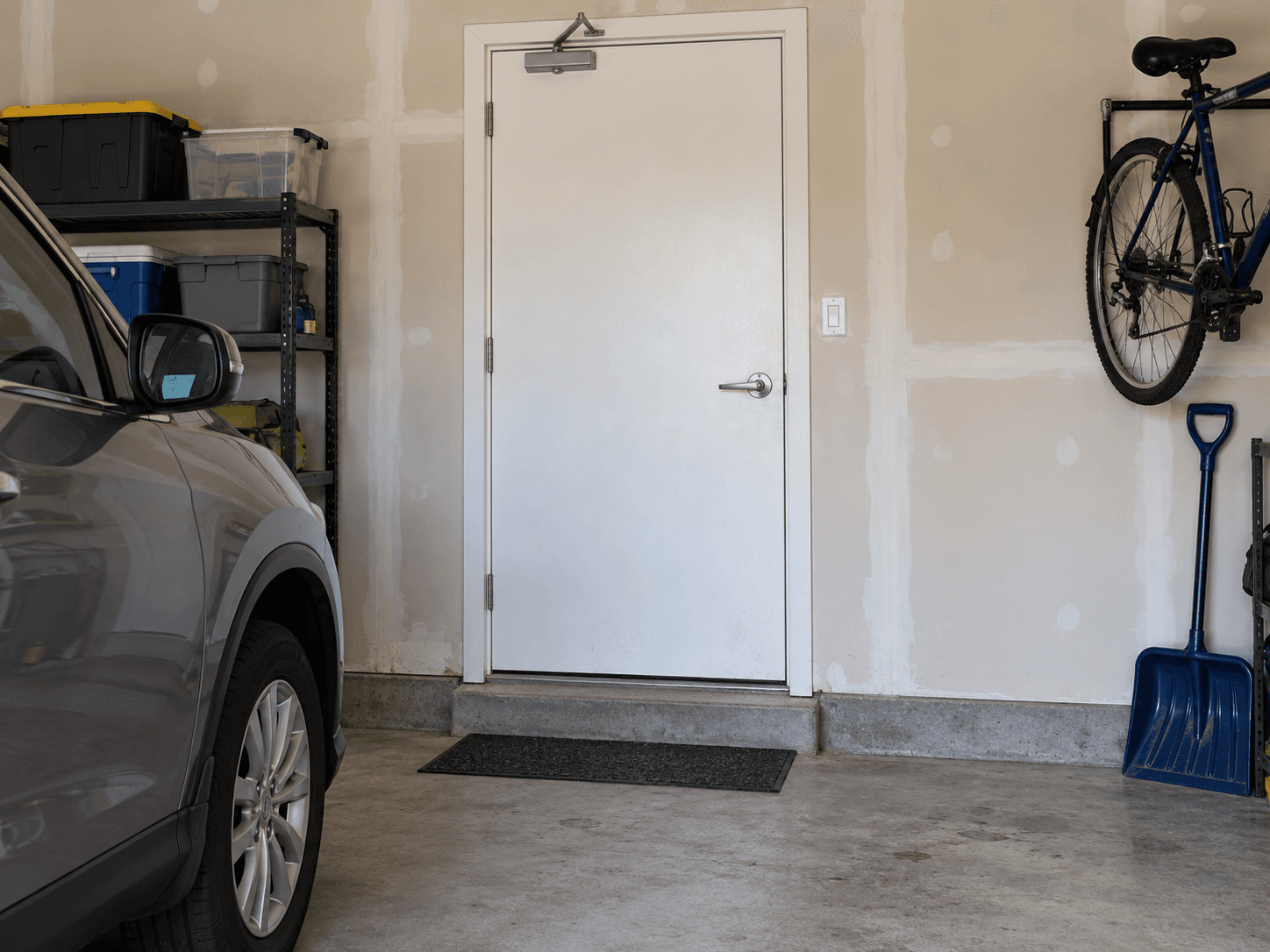 A closed solid door between an attached garage and the house, with a parked car at the edge and a clear threshold.