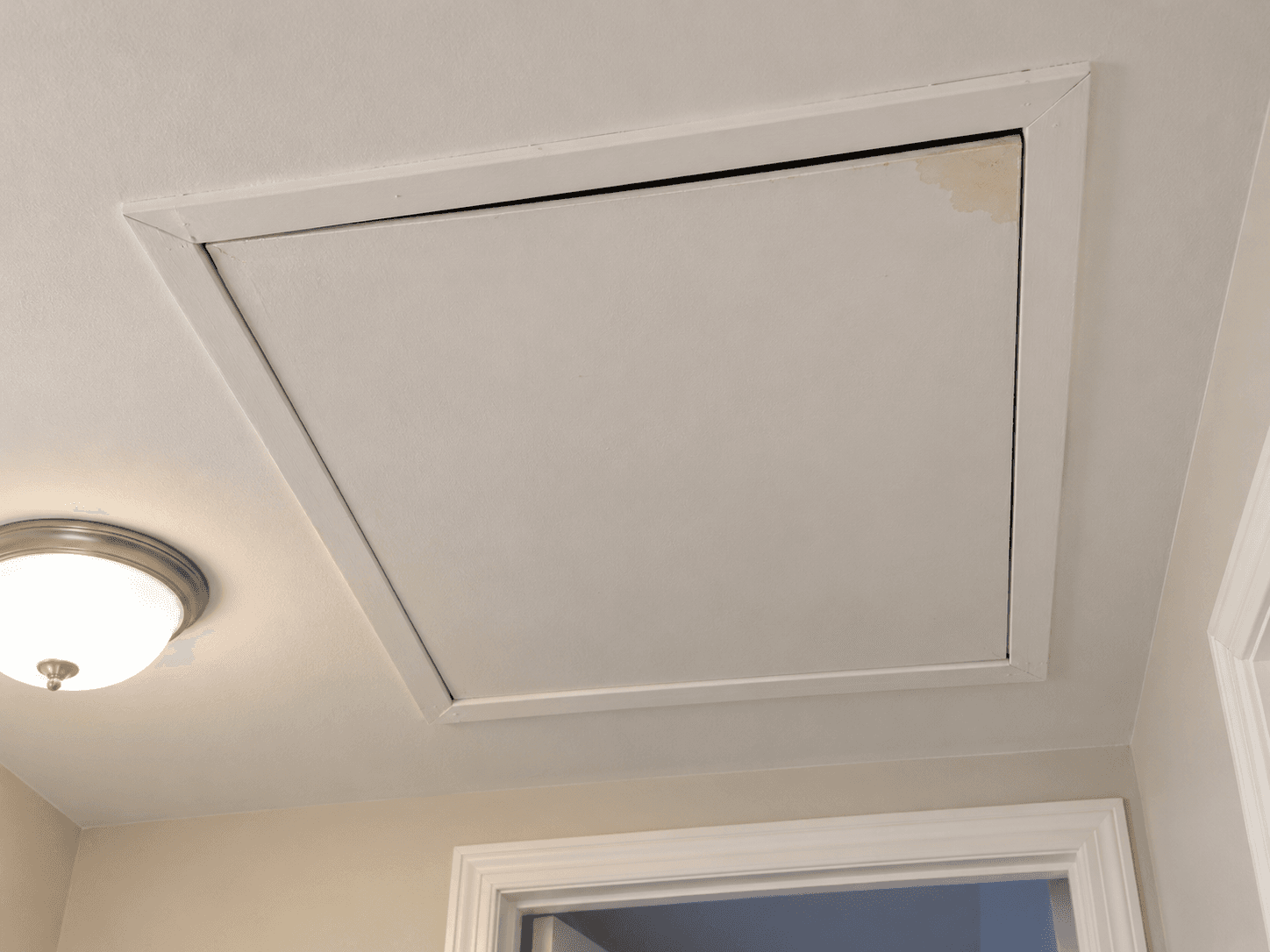 An attic access panel in a hallway ceiling has an uneven edge gap visible from below.