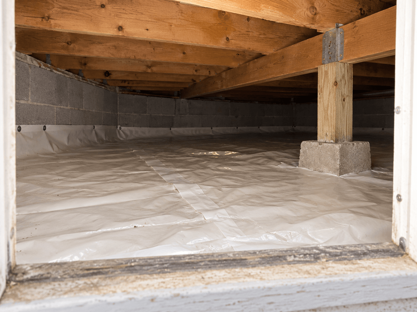 A low crawl space seen from its access opening, with visible floor joists and a ground membrane.