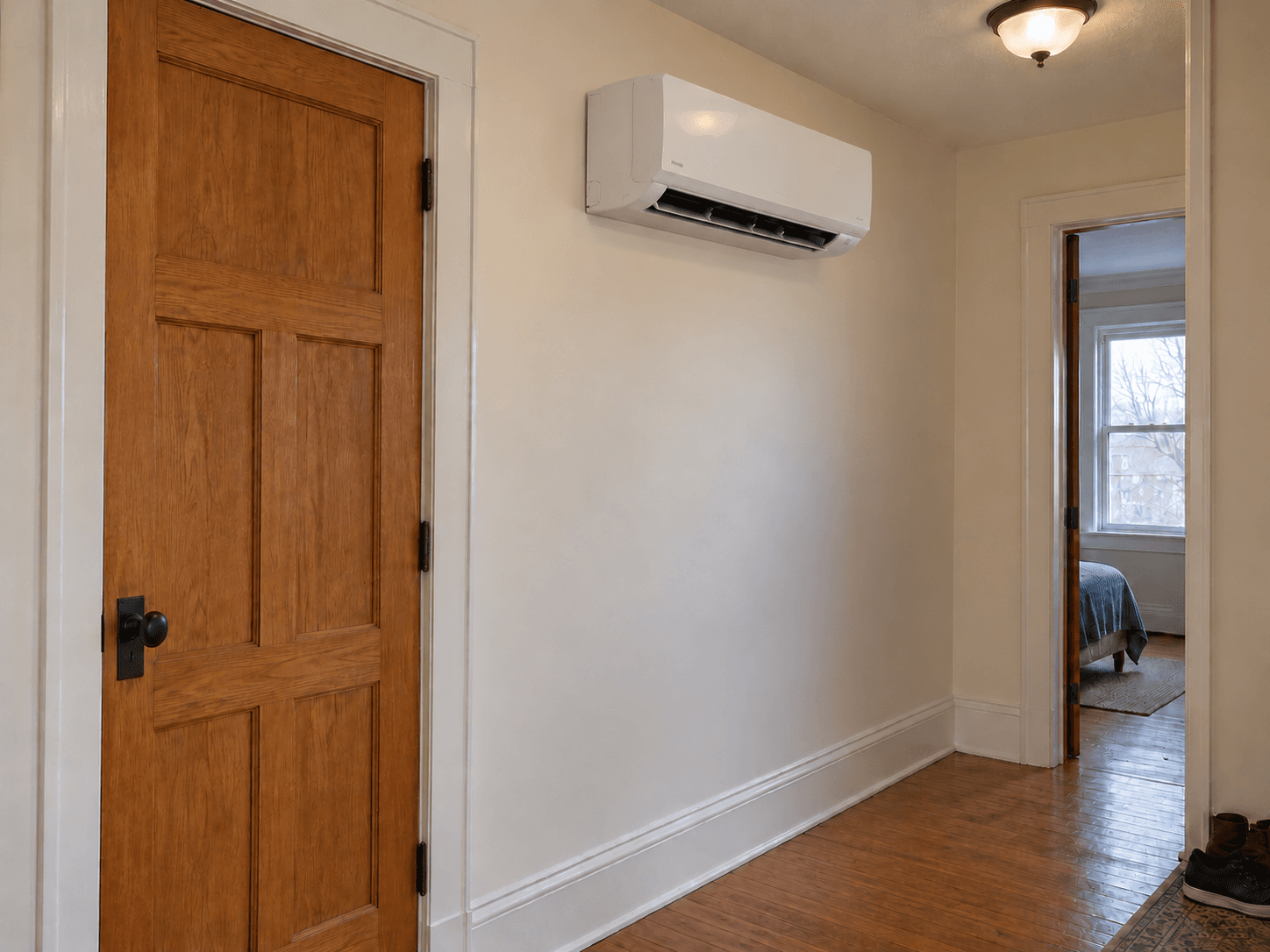 A high wall-mounted ductless head sits in a hallway beside a closed bedroom door.