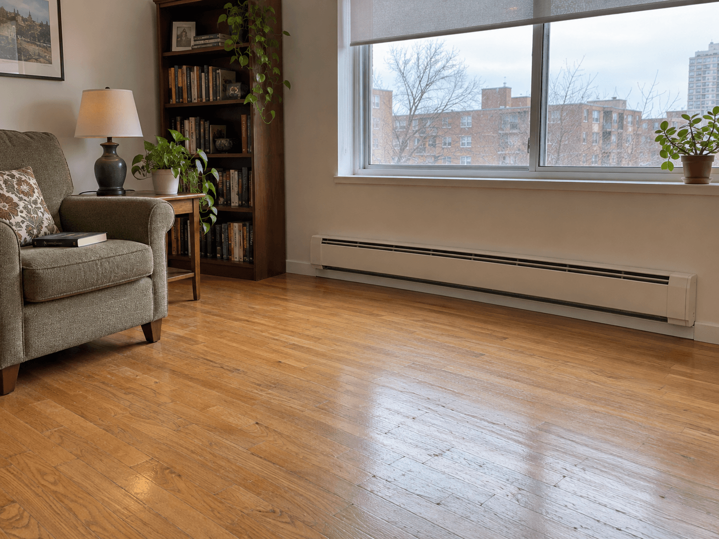 A cream electric baseboard below a roller blind, with open floor in front and an armchair to the side.