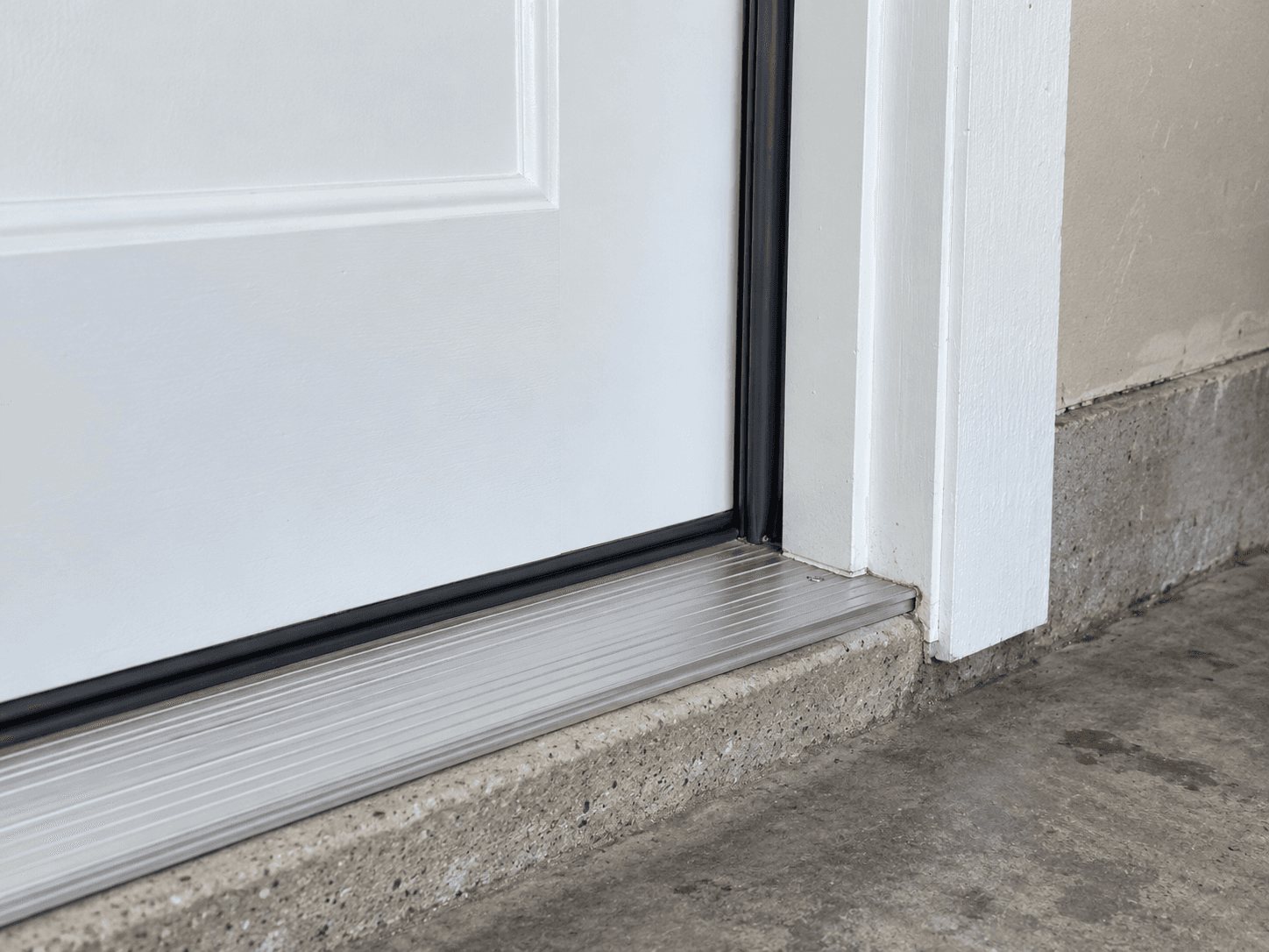 The bottom corner of a solid pedestrian door with continuous seals meeting an aluminium threshold.