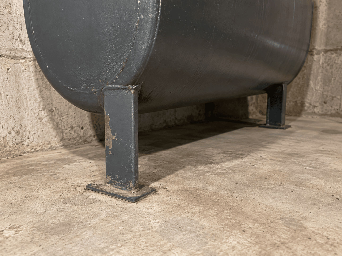 An oil tank's legs and lower fittings above the basement floor.