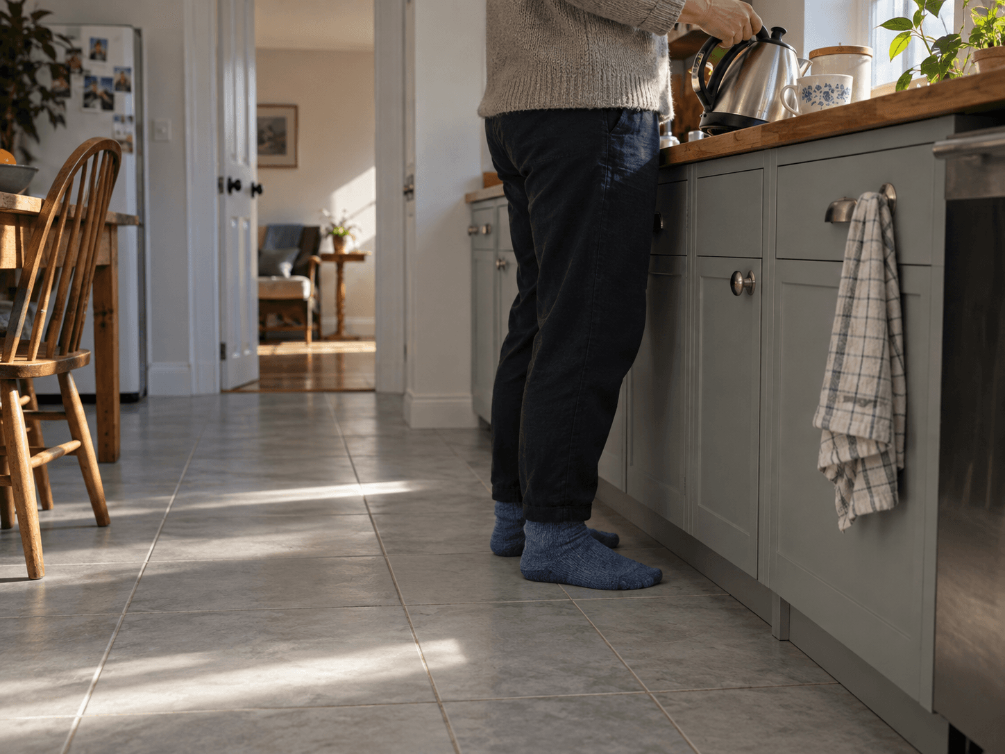 A homeowner in blue socks making tea while standing on a pale tiled kitchen floor.