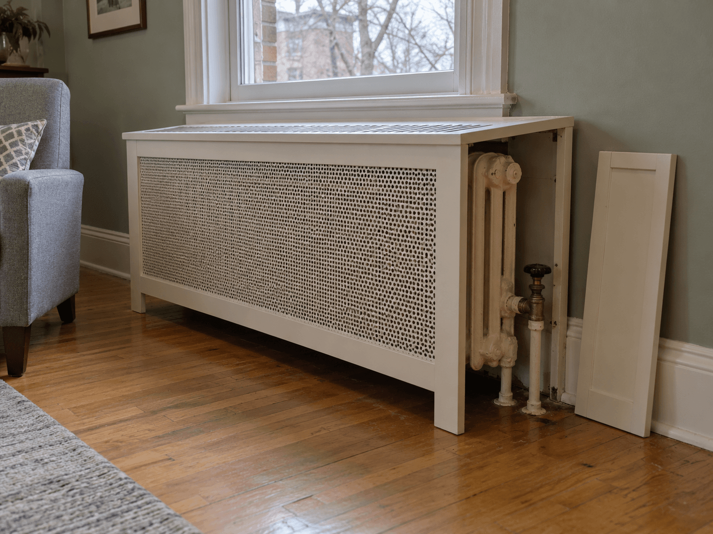 A perforated radiator cover with a slotted top and a removed side panel exposing the radiator valve.