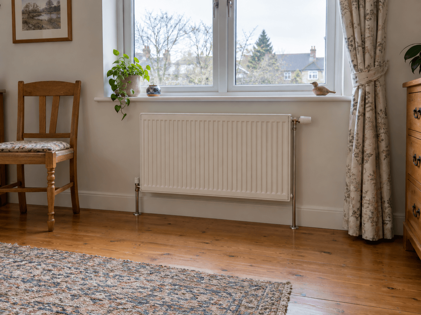 A panel radiator with its thermostat head exposed to the room and the curtain held clear.