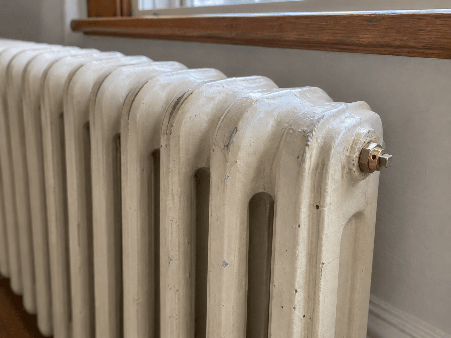 A closed manual bleed fitting at the upper end of an older cast-iron radiator.