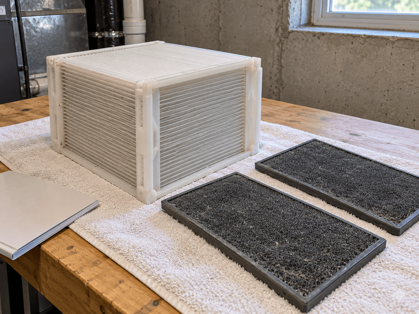A rigid layered plastic recovery core and two separate coarse filter pads resting on a towel in a basement work area.