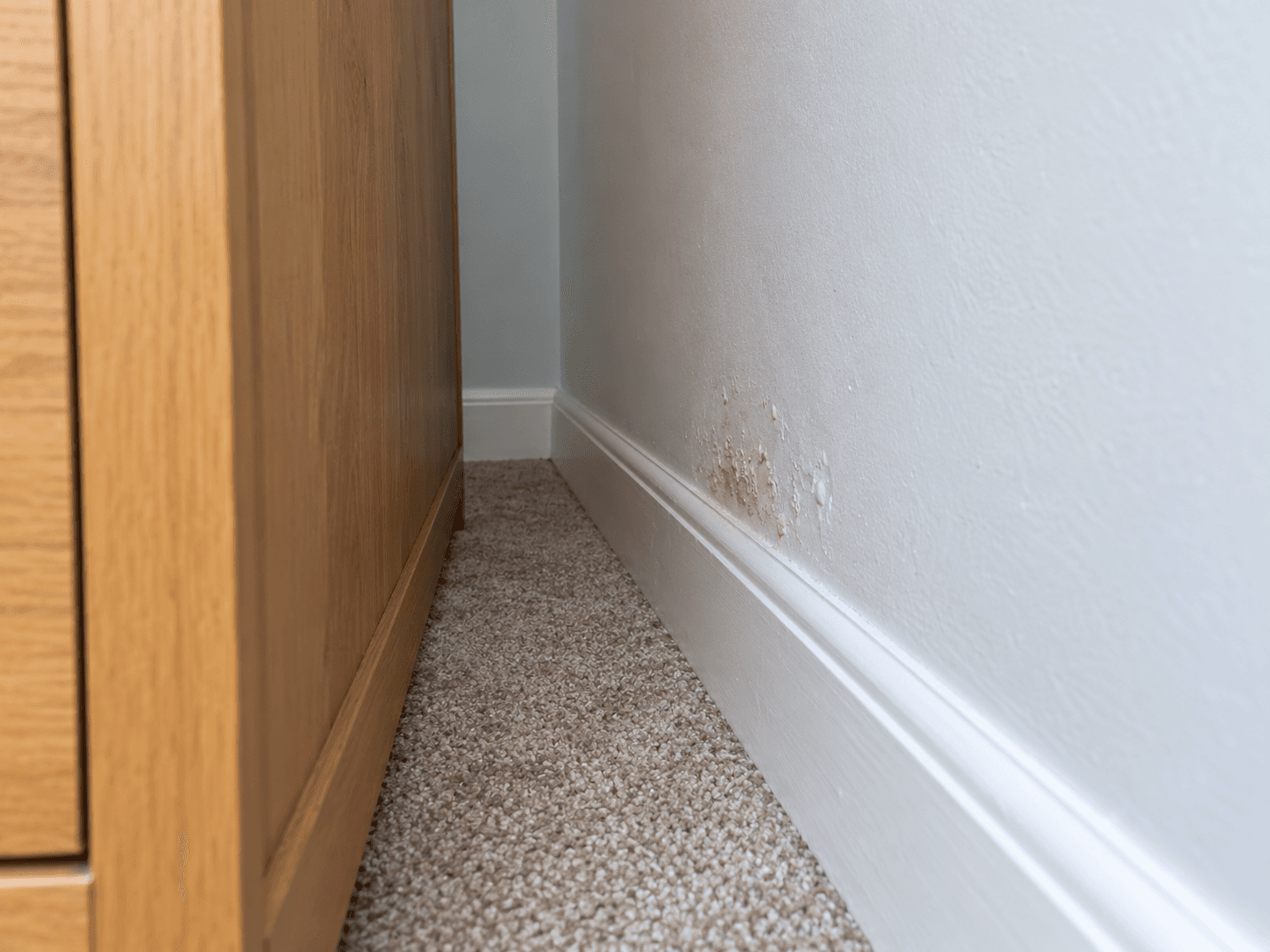 A visible gap behind a stable wardrobe exposes a small patch of damaged paint near the skirting.