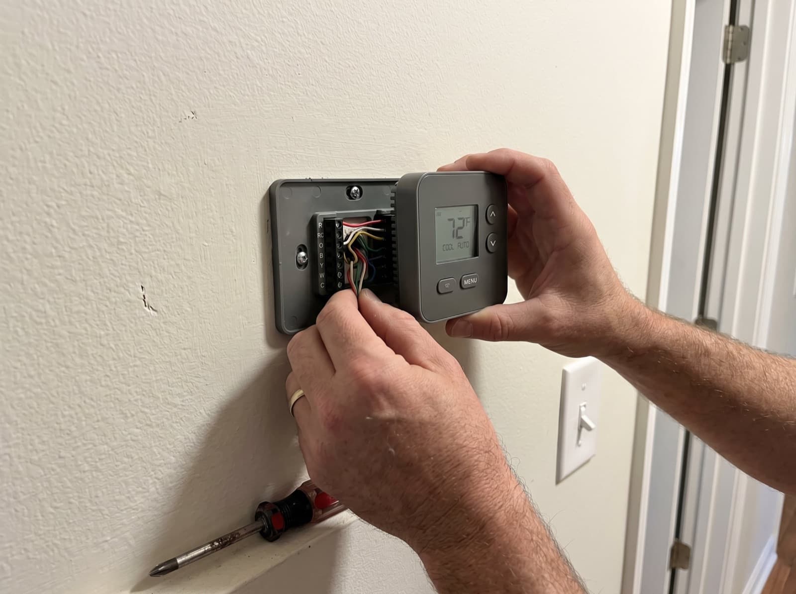 Hands installing and wiring a new digital thermostat.